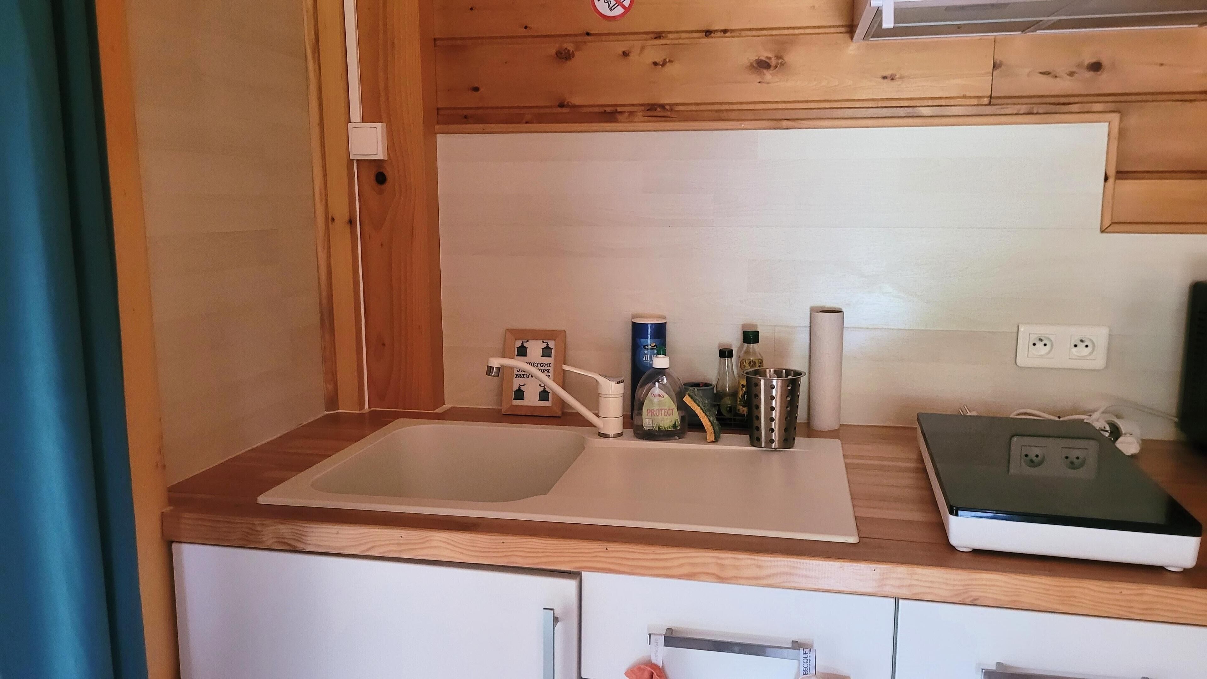 Une cuisine avec un plan de travail en bois, un évier et une balance. On y trouve des bouteilles et un rouleau d’essuie-tout sur le plan de travail.