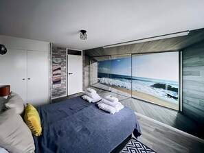Enjoy ocean views from the large bed in this stylish room, featuring a wardrobe, table, and wall-mounted light.