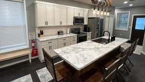 A modern kitchen with white cabinets, a marble island, and a built-in oven.