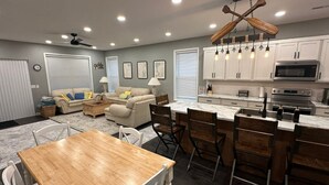 A modern kitchen with white cabinets, a wooden dining table, and a bar area.