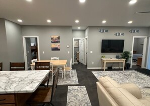 Ein modernes Wohnzimmer mit einer Couch, einem Esstisch mit Stühlen, einem Fernseher und Bildern an den Wänden.