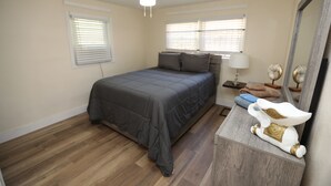 Ein Schlafzimmer mit einem Bett, einem Nachttisch, einer Lampe, einem Deckenventilator und einem Spiegel.