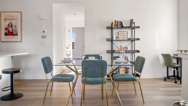 A modern dining area with a glass table, teal chairs, and a bookshelf in the background. - King Bed » Garage » AC » Full Kitchen » 65` (Calgary)