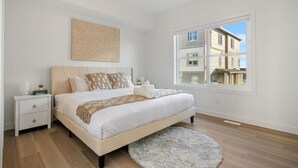 Een slaapkamer met een groot bed, een nachtkastje, een zacht tapijt en een raam met uitzicht op gebouwen.
