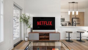 A modern living room with a large flat-screen TV mounted on the wall displaying "NETFLIX". - King Bed » Garage » AC » Full Kitchen » 65` (Calgary)