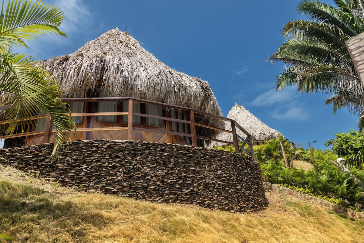 A thatched-roof building with a wooden balcony, surrounded by tropical vegetation.