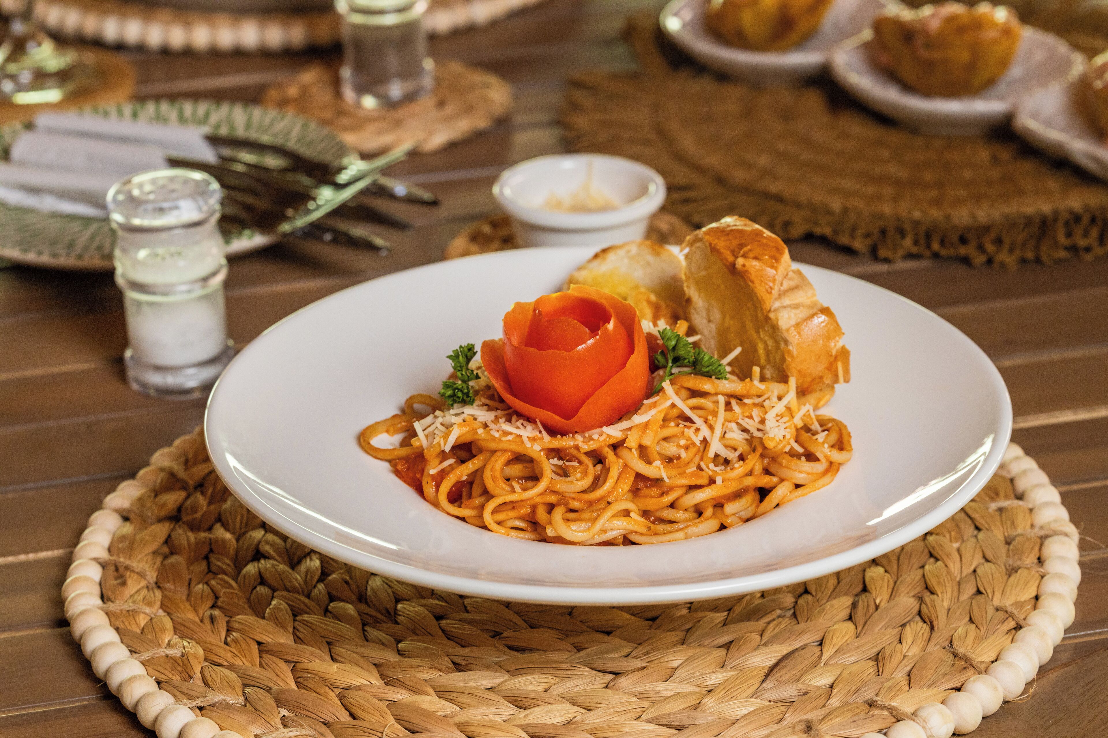 A plate of spaghetti with a rose-shaped garnish and bread on a woven placemat.