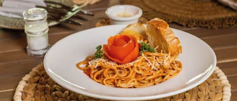 A plate of spaghetti with a rose-shaped garnish and bread on a woven placemat.