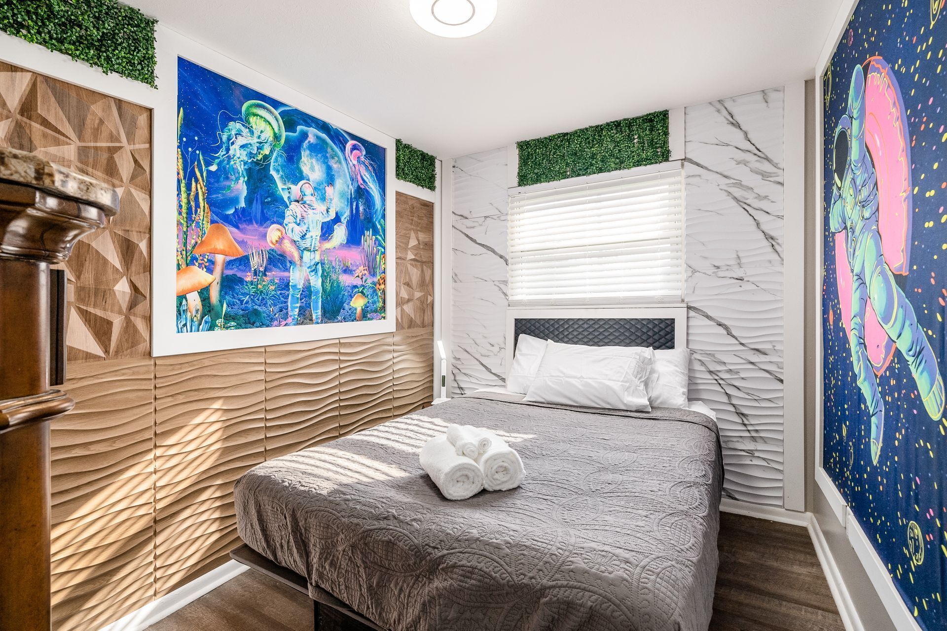 Une chambre à coucher comprenant un lit, une tête de lit, un mur orné d’un motif végétal vert et un grand tableau représentant des méduses et un astronaute.