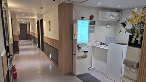 A hotel corridor with a reception desk, a digital screen displaying information, a fire extinguisher, and a water dispenser. - U-Rim Stay (Seoul)