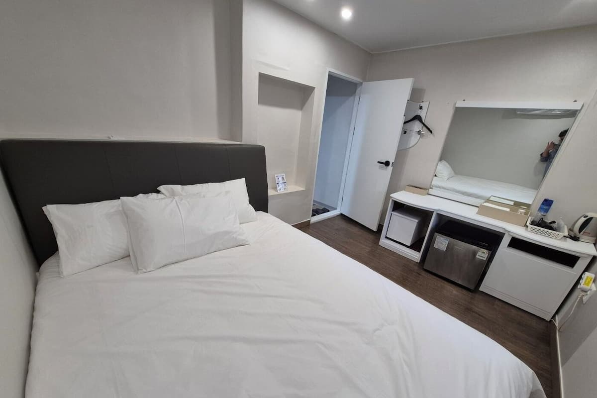 A modern hotel room with a large bed, a small desk, a mirror, and a door leading to a bathroom.
