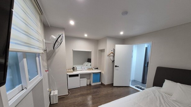 A modern hotel room with a bed, a desk, a mirror, and a window with blinds. - U-Rim Stay (Seoul)