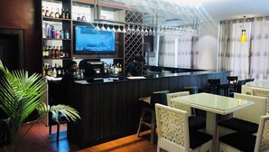 A bar area with a counter, shelves with bottles, and a TV screen. There are chairs and tables in the seating area. - Southern Altantic  Hotels and Apartments (Yenagoa)