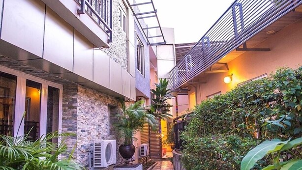 A narrow outdoor corridor with a stone wall, a metal staircase, and a variety of plants. - Southern Altantic  Hotels and Apartments (Yenagoa)