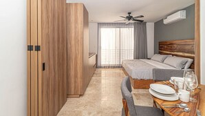 A modern bedroom with a bed, a desk, and a dining table set with plates and glasses. - King Studio w/ Private Balcony + Rooftop Pool, Gym (Tulum)