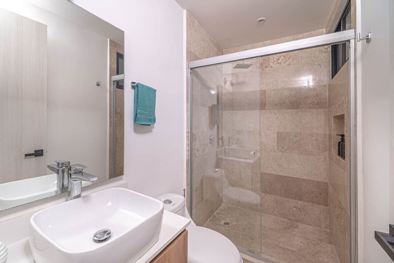 A modern bathroom with a large sink, mirror, and glass-enclosed shower.