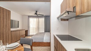 A compact hotel room with a kitchenette, a bed, a dining area, and a ceiling fan. - King Studio w/ Private Balcony + Rooftop Pool, Gym (Tulum)