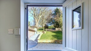 A door leading to a garden with a paved path, a brick wall, and a grassy area with trees.