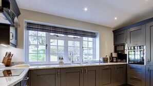 A modern kitchen with dark cabinetry, a large window with blinds, and stainless steel appliances.