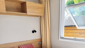 Un dormitori amb un llit, dues almoines, un capçal de fusta, una tauleta de nit, una làmpada penjada a la paret, una finestra amb cortines i un finestral.