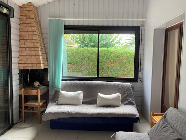A small, cozy room with a bed, a chair, and a window overlooking a garden.