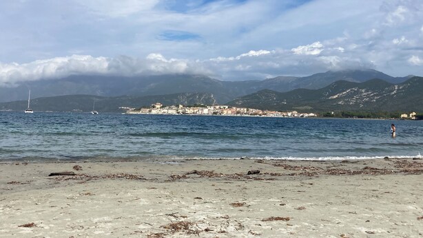 Une plage avec vue sur une ville côtière et des montagnes en arrière-plan.