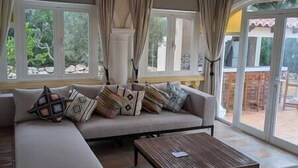 A living room with a sofa, a coffee table, and large windows with curtains. - Villa Carolina. Costa Nova, Jávea (Xàbia)