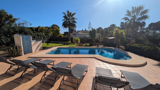 A swimming pool with a tiled deck, surrounded by palm trees and a well-maintained lawn. - Villa Carolina. Costa Nova, Jávea (Xàbia)