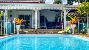 A swimming pool with two sun loungers, a covered patio area with outdoor furniture, and potted plants. - Villa Horizon Caraïbes (Petit-Bourg)