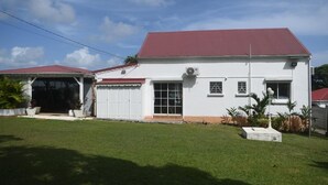 A white building with a red roof, a garage, and a well-maintained lawn. - Villa Horizon Caraïbes (Petit-Bourg)