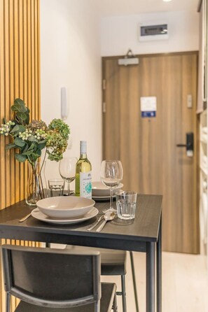 A dining table set with plates, glasses, and a bottle of wine, with a wooden panel and a door in the background. - Prądnik Czerwony Studio - Balcony, City View - by Rentujemy (Kraków)