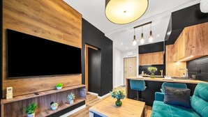 Un salon moderne doté d’un grand téléviseur à écran plat, d’étagères en bois ornées de plantes, d’une table à manger et d’un canapé de couleur turquoise.