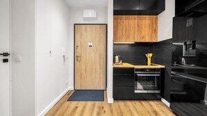 Une cuisine de taille réduite, dotée d’appareils électroménagers noirs, d’une porte en bois et d’un revêtement mural noir.