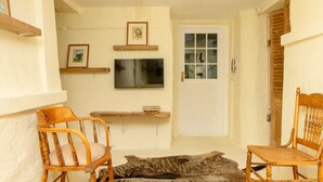 A cozy room with a wooden chair, a small table, a TV mounted on the wall, and a white door.