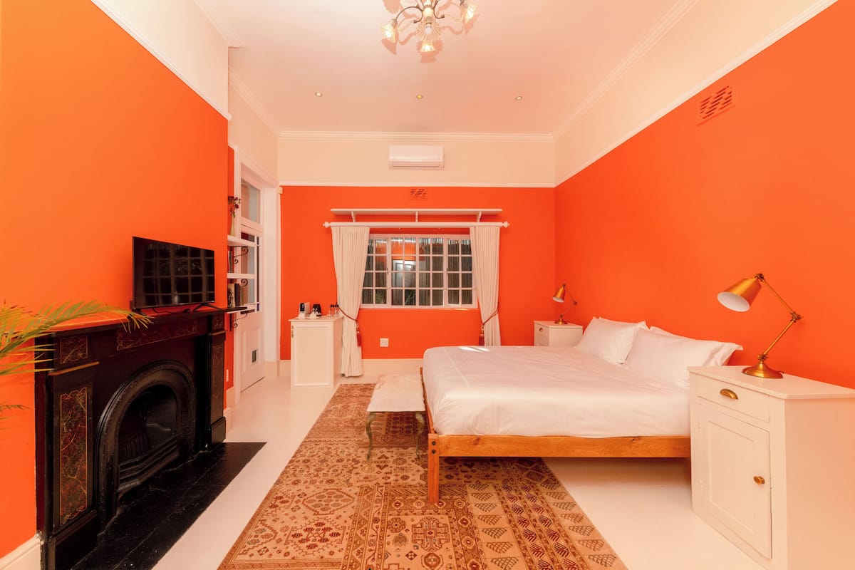 Une chambre à coucher avec un grand lit, une cheminée, une fenêtre avec des rideaux et une table de chevet avec une lampe.