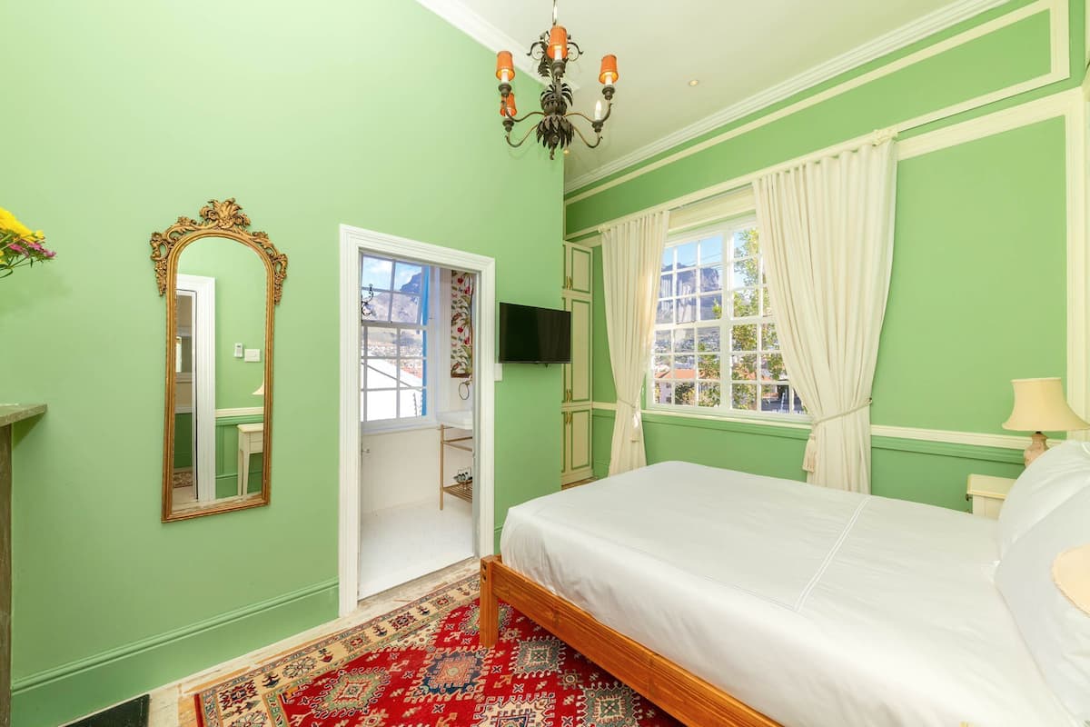 Une chambre à coucher avec un lit, un miroir, un lustre, une télévision et une fenêtre avec des rideaux.