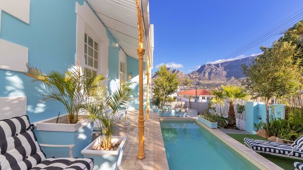A pool area with a blue building, outdoor seating, and a mountain view.