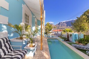 Un espace piscine avec un bâtiment bleu, des sièges en plein air et une vue sur la montagne.
