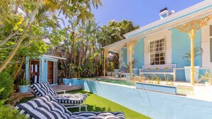 A pool area with lounge chairs and a small building with a blue exterior.