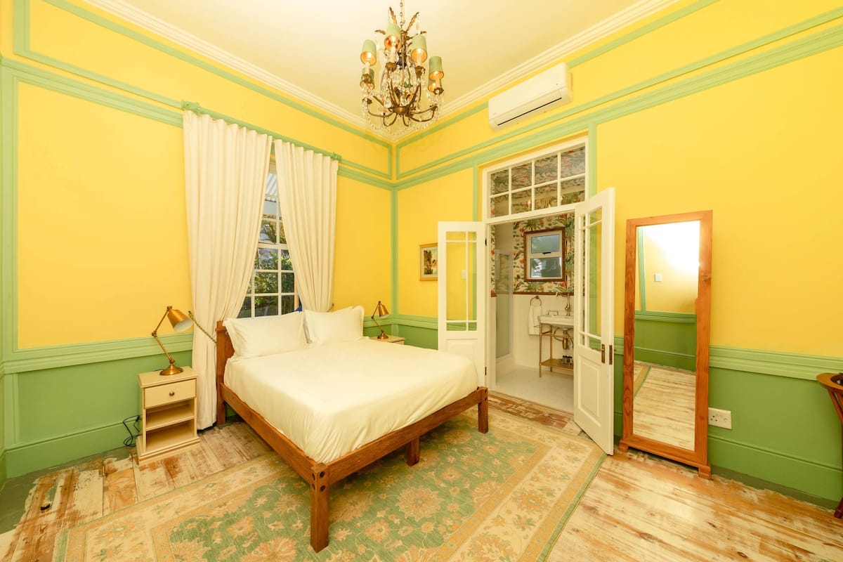 Une chambre à coucher comprenant un lit, une table de chevet, un lustre et une porte donnant sur une autre pièce.