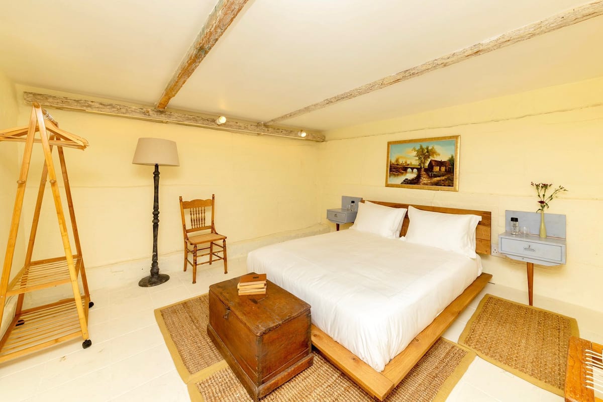 Une chambre à coucher avec un lit en bois, une commode en bois, une chaise, une lampe et un tableau accroché au mur.