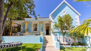 A light blue house with a covered porch, steps leading to the entrance, and a small patio area with a table and chairs.