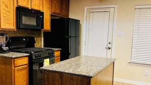 A kitchen with wooden cabinets, a black refrigerator, a microwave, a stove, and a granite countertop island. - Cozy Home in Spring,TX with AC /WiFi / Laundry . 20 mins from IAH Airport (Spring)