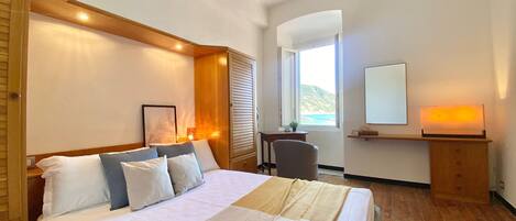 Una camera da letto con un letto, una scrivania, una sedia, uno specchio e una finestra vista mare.