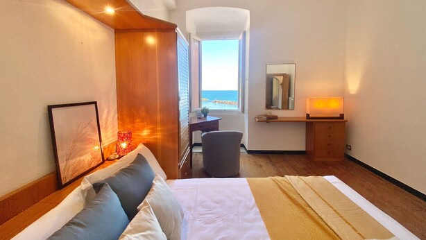A hotel room with a bed, bedside table, chair, desk, and a view of the sea. - La Spiaggia (Moneglia)