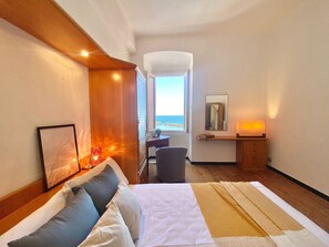 A hotel room with a bed, bedside table, chair, desk, and a view of the sea. - La Spiaggia (Moneglia)