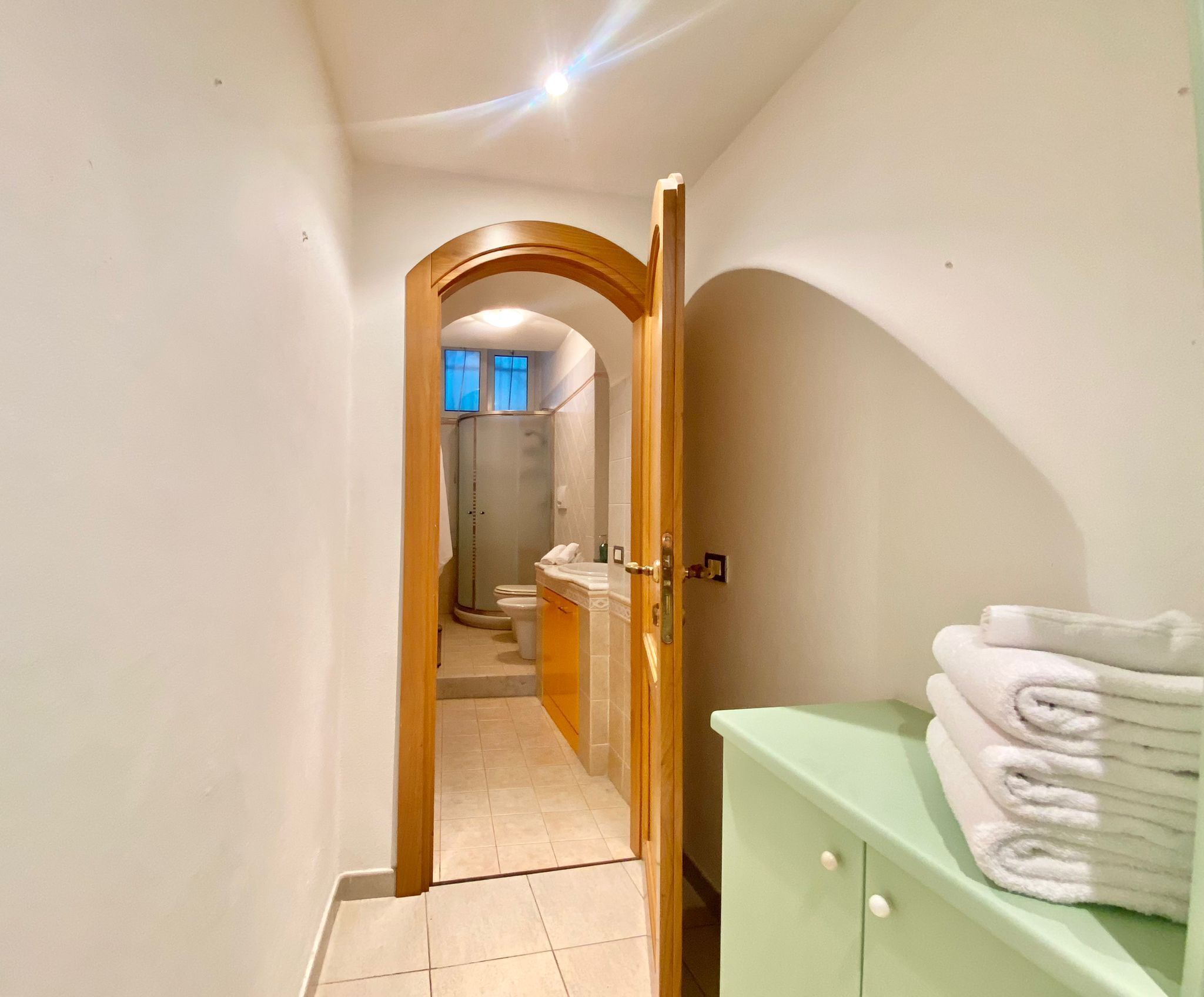 Un pasillo estrecho que conduce a un baño con ducha, inodoro y lavamanos.