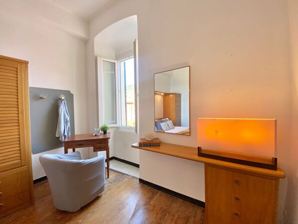 A bedroom with a wooden bed, a bedside table, a chair, a desk, a mirror, and a window. - La Spiaggia (Moneglia)