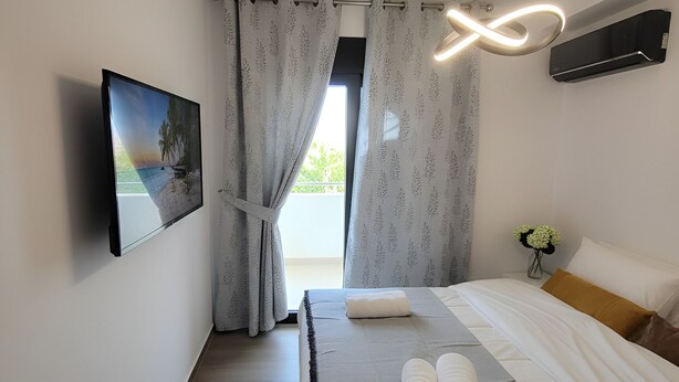 Une chambre moderne avec un lit, des rideaux, un climatiseur fixé au mur, une table de chevet avec un vase de fleurs et un tableau accroché au mur.