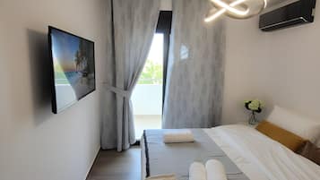 Une chambre moderne avec un lit, des rideaux, un climatiseur fixé au mur, une table de chevet avec un vase de fleurs et un tableau accroché au mur.